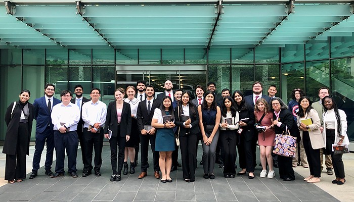 A group of nicely dressed people stand in front of a modern green glass building.